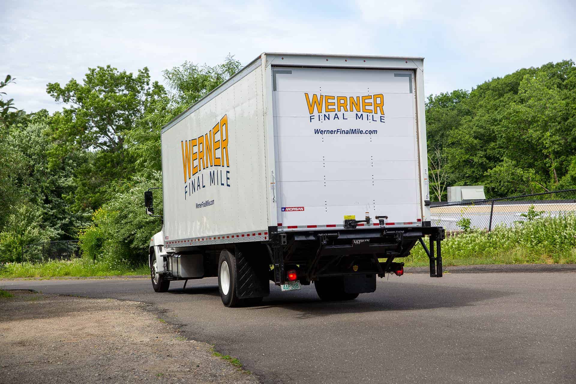 Werner Final Mile straight truck with a liftgate, seen from behind on a tree-lined road