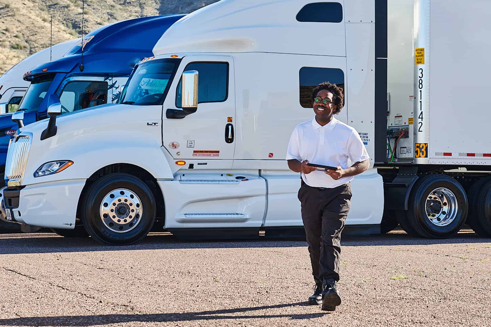 Driver carrying a tablet walks past a row of white and blue tractors